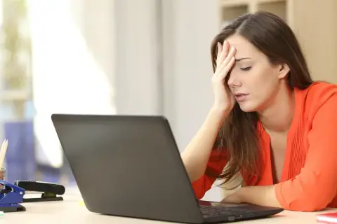 A woman with her hand on her forehead, looking stressed at her laptop, likely after being passed over for promotion.