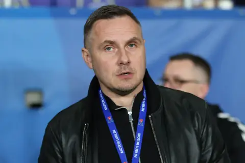Mężczyzna w czarnej kurtce z niebieską smyczą z napisem "MOTOR LUBLIN" na szyi.