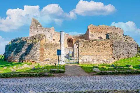 Ruines antiques sur l'Appia Antica à Rome, sous un ciel bleu parsemé de nuages blancs.