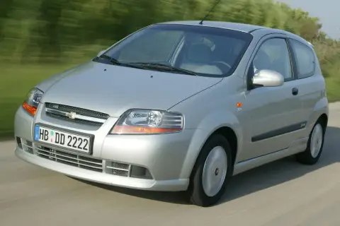 Srebrny Chevrolet Kalos w wersji 3-drzwiowej jedzie po drodze, rozmyte tło sugeruje ruch.