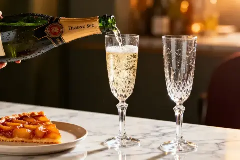 Une coupe de tarte aux fruits caramélisés est servie avec un verre de vin de dessert pétillant, versé d'une bouteille de champagne.