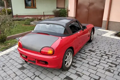 Czerwone Suzuki Cappuccino z czarnym dachem i maską stoi na podjeździe z kostki brukowej.