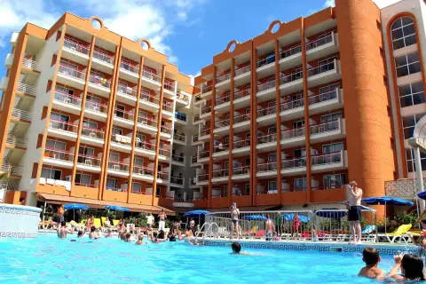 Gente disfrutando en la piscina del hotel Belvedere Salou, con edificios naranjas y blancos de fondo.