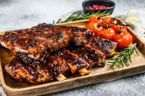Pyszne żeberka cielęce w sosie barbecue, podane z pieczonymi pomidorkami i rozmarynem. Idealny przepis na obiad.