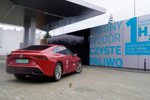 Czerwona Toyota Mirai na stacji tankowania wodoru. "Zielony wodór, czyste paliwo" - hasła na budynku stacji.