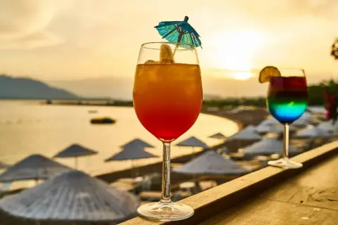 Dwa kolorowe drinki na tle plaży i zachodzącego słońca.