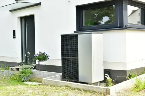 Pompa ciepła zainstalowana przy nowoczesnym domu z białym tynkiem i dużym oknem.