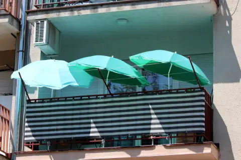 Trzy turkusowe parasole nad zasłoniętą balustradą na balkonie. Pomysł, jak zasłonić balustradę na balkonie, wykorzystując parasole.