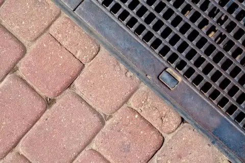 Kostka brukowa i metalowa kratka ściekowa zapewniające sprawne odwodnienie domu.