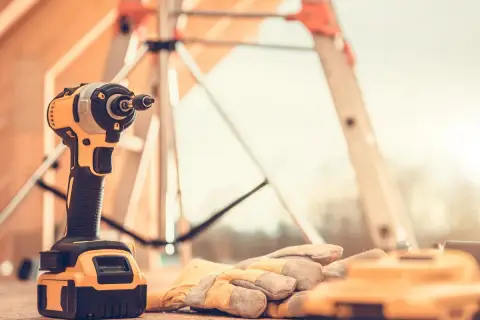 Wkrętarka i rękawice robocze leżą na desce. To niezbędne narzędzia na budowę, gotowe do pracy.