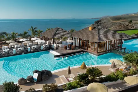 Un resort todo incluido con piscinas cristalinas, palmeras y vistas al mar. Mesas al aire libre y un bar acuático invitan a relajarse bajo el sol.