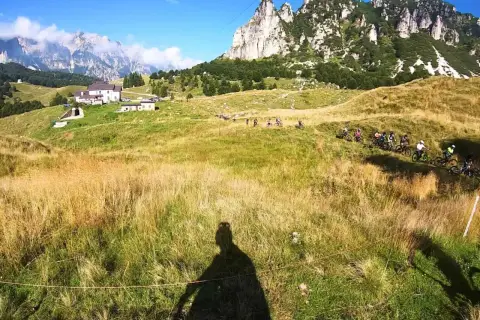 Gruppo di ciclisti in discesa su un sentiero erboso, con montagne imponenti sullo sfondo. Un'avventura a Recoaro 1000.