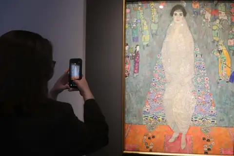 Besucherin fotografiert das größte Gemälde der Welt, ein detailreiches Porträt einer Frau in einem opulenten Kleid, umgeben von bunten Figuren.