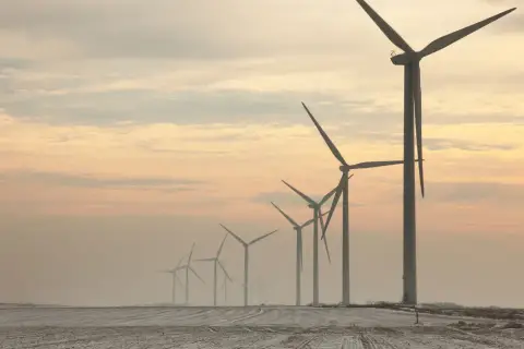 Rząd potężnych farm wiatrowych na tle zachodzącego słońca, tworzący malowniczy krajobraz.
