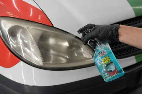 Mano guantata spruzza detergente su un faro opaco. La lucidatura fari quanto dura dipende dal metodo, ma un buon prodotto può fare miracoli.