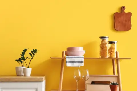 Cucina con pareti giallo vivace, dove **vernici naturali** esaltano gli arredi: piante, pasta in barattoli, piatti rosa e un tagliere in legno.
