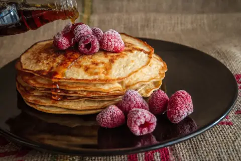 Pila de tortitas doradas con frambuesas congeladas y sirope cayendo. Una deliciosa receta de tortitas para disfrutar.