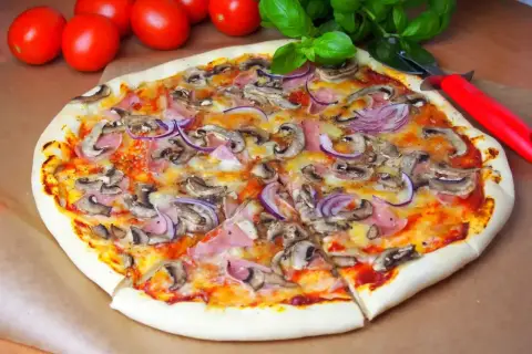 Pyszna pizza capriciosa z pieczarkami, szynką i czerwoną cebulą, gotowa do pokrojenia.
