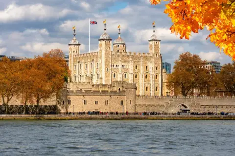 Jesienna panorama Londynu z twierdzą Tower i rzeką Tamizą. Liście drzew mienią się złotem.