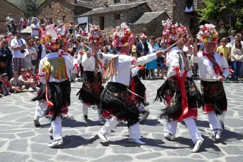 Hombres con trajes tradicionales y sombreros florales bailan en la plaza durante el **Día del Corpus**.