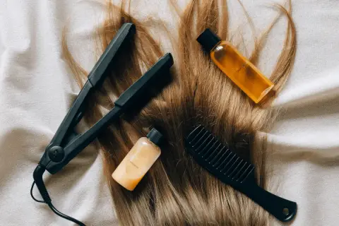 Plancha, peine y botellitas de champú y acondicionador sobre cabello rubio. Una solución casera para el pelo naranja.