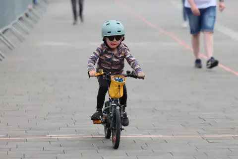 Małe dziecko w kasku i okularach przeciwsłonecznych śmiga na rowerze, wyciągając język. To dziecko na rowerze przepisy, jak prawdziwy mistrz.