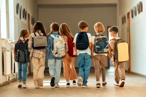 Dzieci z plecakami idą korytarzem. Czas na wystawienie ocen na 1 semestr!