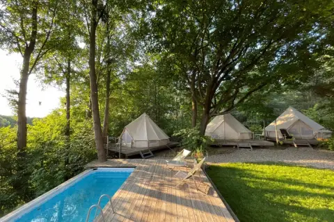 Luksusowy glamping nad jeziorem: namioty tipi na drewnianych tarasach, basen i leżaki wśród drzew. Idealne miejsce na relaks.