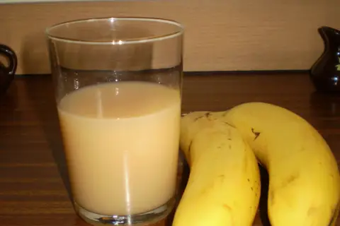 Szklanka orzeźwiającego soku z banana obok dwóch dojrzałych bananów. Idealny napój na szybkie śniadanie.