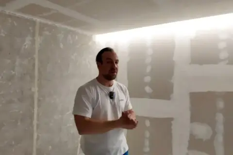 Mężczyzna prezentuje sufit podwieszany z wnęką na led, w trakcie prac wykończeniowych.
