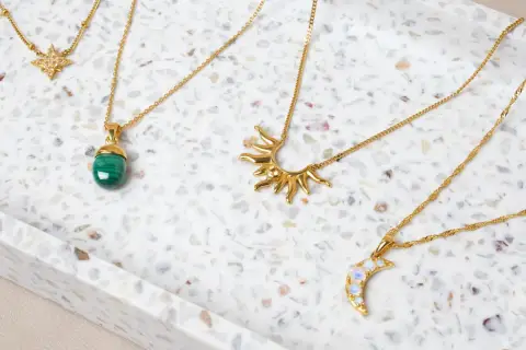 Fyra guldfärgade halsband med olika hängen: en stjärna, en grön sten, en sol och en måne. Vilken kristall passar mig?