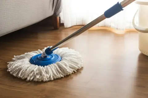 Mop na drewnianej podłodze, obok wiaderka. Idealny do pytania: czym myć panele.