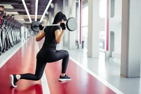 Kobieta wykonuje wykroki ze sztangą. Efektywny trening siłowy dla kobiet.