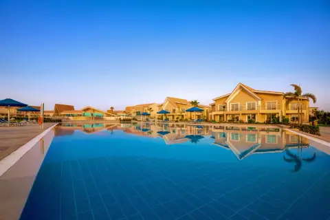 Basen hotelowy w Pickalbatros Sea World Marsa Alam z odbijającymi się w wodzie budynkami i palmami.