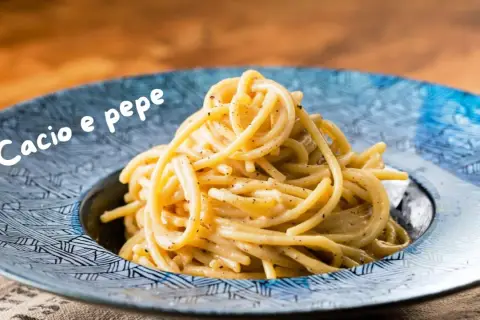 Un piatto di spaghetti fumanti, conditi con una cremosa salsa cacio e pepe, serviti in un piatto blu decorato.
