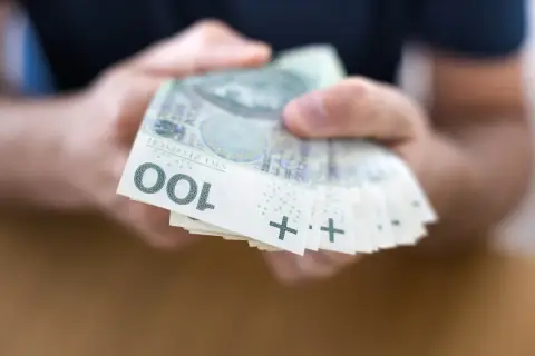 Dłonie trzymają stos banknotów 100 zł. To może być początek drogi do finansowej stabilności, jak kasa stefczyka konsolidacja.