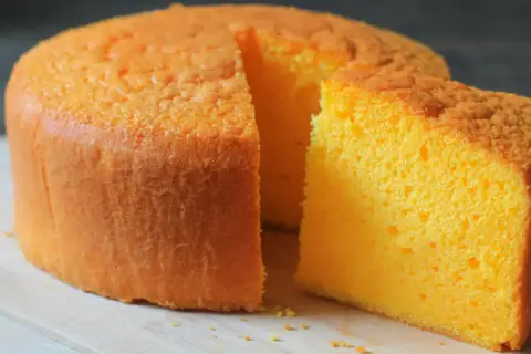 Puszysty, pomarańczowy tort z widocznym kawałkiem ciasta, gotowy do podania.