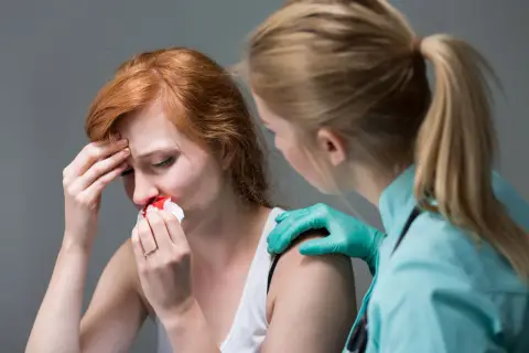 Kobieta z krwawiącym nosem, trzymająca chusteczkę. Obok stoi osoba w rękawiczkach, która ją wspiera. Czy to objaw APTT?