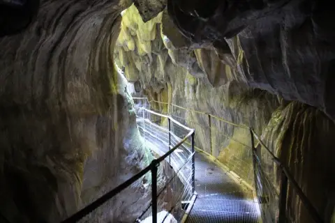 Pasarela metálica serpentea por el interior de los Gorges de la Fou, con paredes rocosas esculpidas por el agua y la luz filtrándose desde arriba.