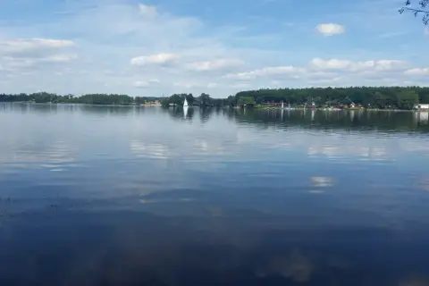 Spokojne **jezioro Pławniowice** z odbijającymi się chmurami i żaglówkami na horyzoncie.