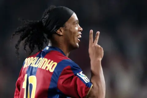 Piłkarz Ronaldinho w koszulce Barcelony, z charakterystyczną opaską na głowie i kucykiem, pokazuje dwa palce. Ile Ronaldinho ma lat?