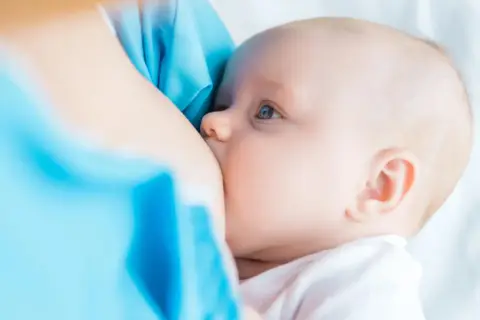 Un neonato si nutre al seno. La domanda su quanto deve mangiare un neonato è comune tra i neogenitori.