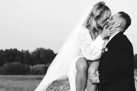 Patrycja Markowska i jej mąż w czułym uścisku na tle wiejskiego krajobrazu.