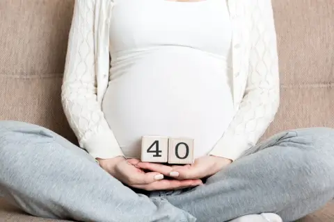Ciąża trwa 40 tygodni. Kobieta w ciąży trzyma w dłoniach kostki z cyframi 4 i 0.