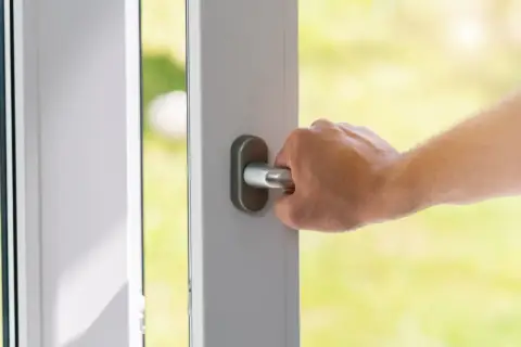 Dłoń chwyta metalową gałkę drzwi, otwierając je na zielony ogród.