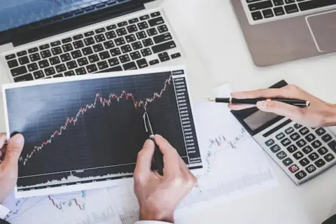 Analiza wykresów akcji co to jest? Dłonie wskazują na wzrosty na papierze wartościowym, obok kalkulator i laptop.