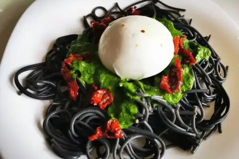 Czarny makaron z zielonym pesto, suszonymi pomidorami i kulką mozzarelli. Wygląda apetycznie!