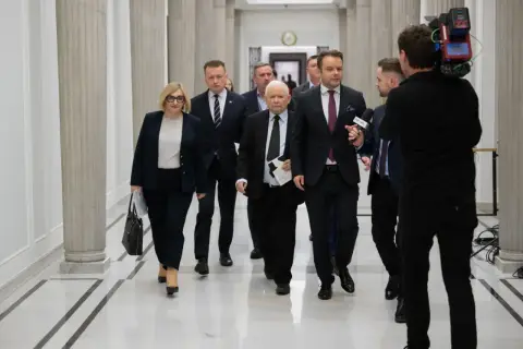 Politycy idą korytarzem, a kamerzysta nagrywa ich z tyłu. Widać, że idą w przeciwnych kierunkach, co jest ciekawe.