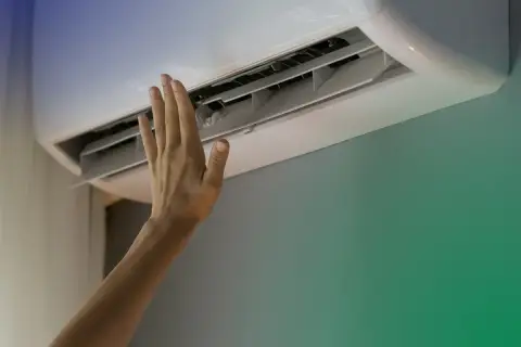 Dłoń dotyka otwartej klimatyzacji ściennej.