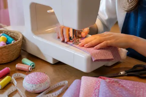 Mains expertes guidant le tissu pour faire des plis précis sur la machine à coudre. Bobines de fil, ciseaux et mètre ruban à proximité.